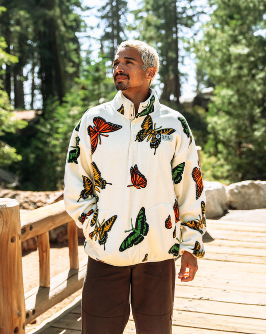 A man wearing a cream fleece pullover jacket with a vibrant multicolor butterfly print, standing on a wooden boardwalk surrounded by a lush green forest.

Shop Butterflies Trail Fleece Inspired by National Parks | cream