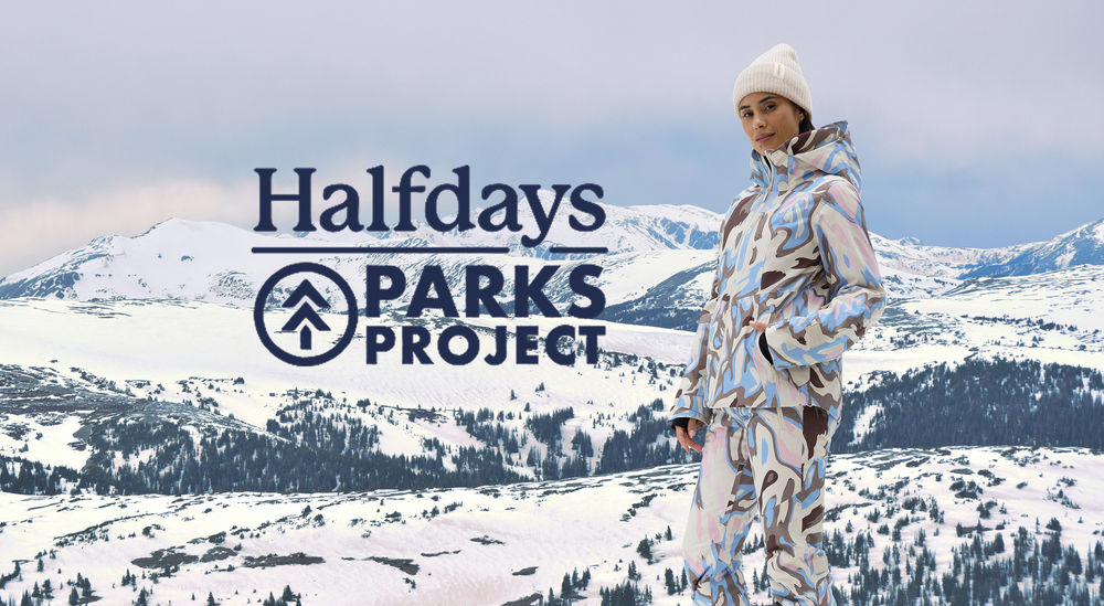 Lady in a full match ski suit from Halfdays x Parks Project logo overlay saying Halfdays x Parks Project. All over print inspired by the Rockies. Nice snowy landscape background
