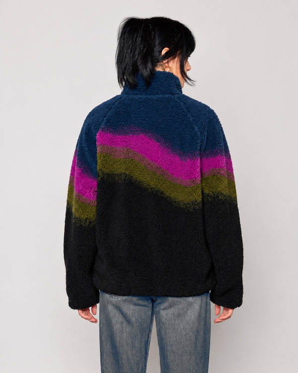 A person viewed from the back wearing a fuzzy quarter-zip fleece jacket with a wavy color-block pattern in navy, magenta, olive green, and black, paired with blue jeans against a light gray studio background.

Shop Borealis High Pile Fleece Jacket Inspired by Alaskan Parks | multi-color